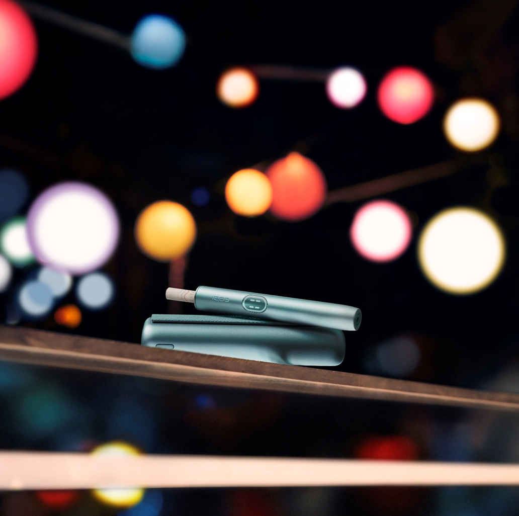 An IQOS ILUMA PRIME Holder with a TEREA stick inserted next to an IQOS ILUMA Pocket Charger.