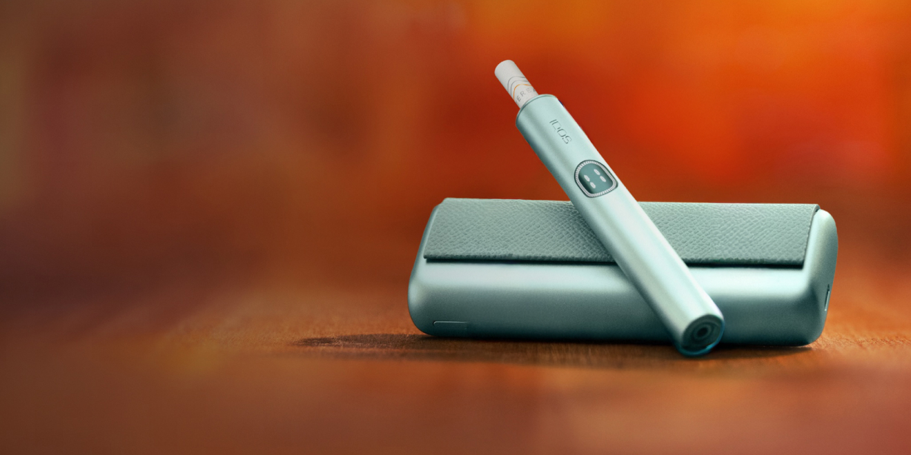 An IQOS ILUMA PRIME Holder with a TEREA stick inserted next to an IQOS ILUMA Pocket Charger.