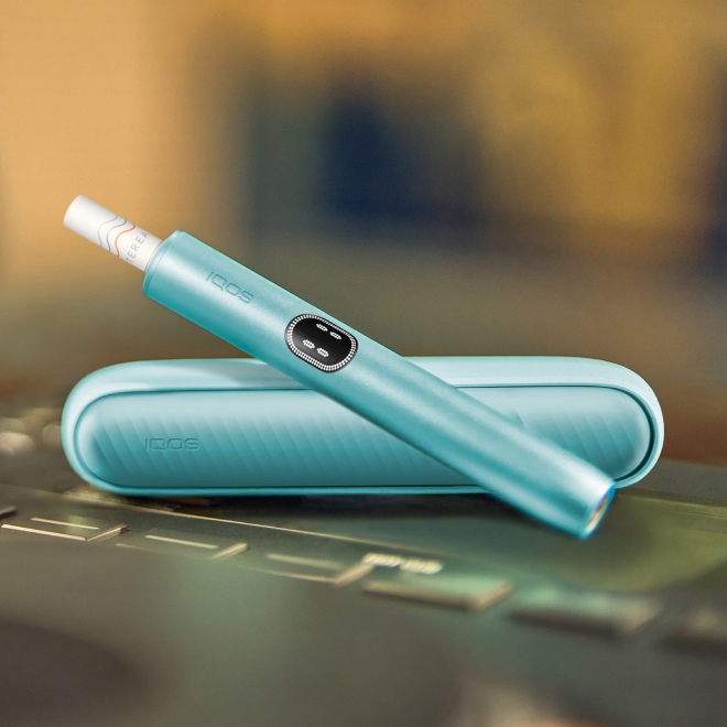 An IQOS ILUMA PRIME Holder with a TEREA stick inserted next to an IQOS ILUMA Pocket Charger.