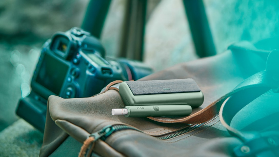 A moss green IQOS ILUMA device with Terea stick next to photography equipment.