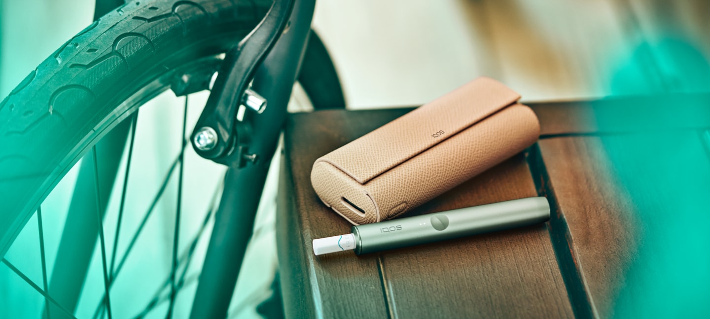 A jade green IQOS ILUMA Prime device on a table, next to a bicycle.