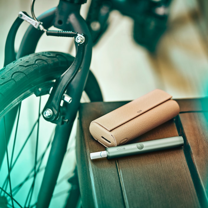 An IQOS ILUMA on a table next to a bicycle.