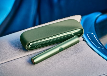 צילום תקריב של IQOS ILUMA בצבע ירוק- מטען נייד ומחזיק.