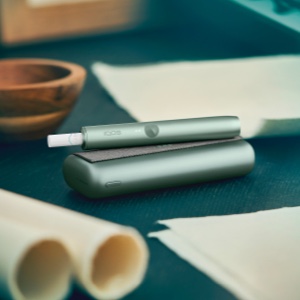 An IQOS ILUMA PRIME device next to pieces of paper.