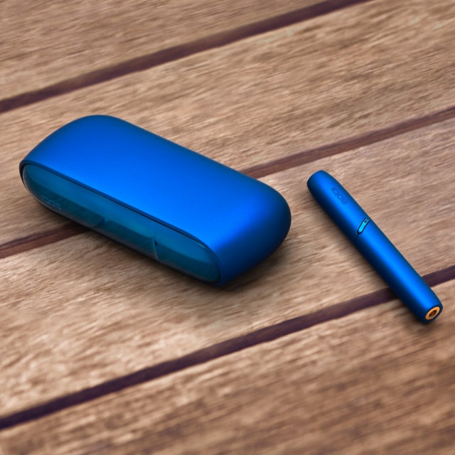 Woman dancing and smiling with a stellar blue IQOS 3 DUO holder in her hand.
