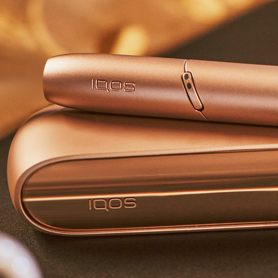 Girl checking her phone at a bar with a IQOS device on the table and the luggage next to her