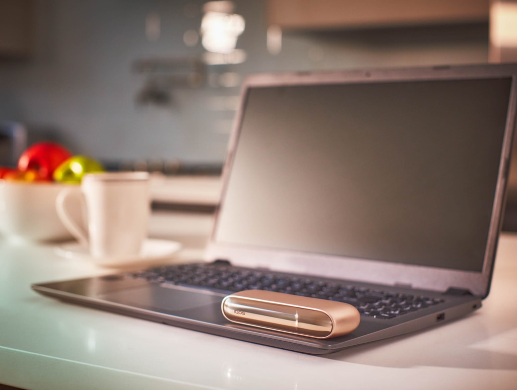Blond woman checking her phone with a IQOS device on the table