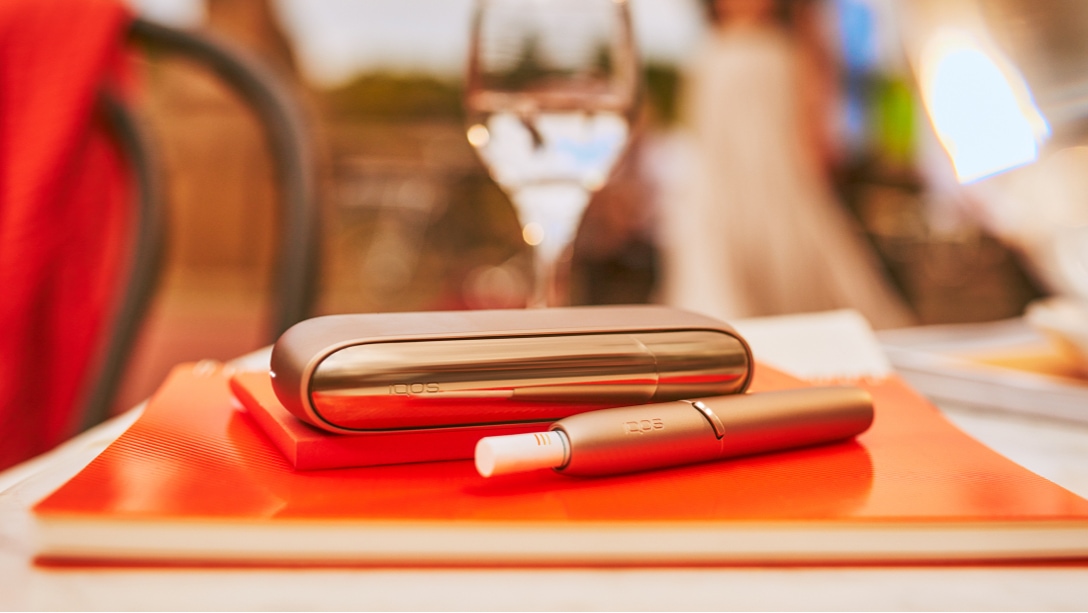 A gold IQOS device next to a bowl of fruit.