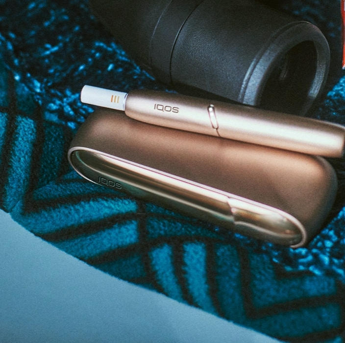 Brilliant gold IQOS 3 DUO with HEETS stick in hand and charger