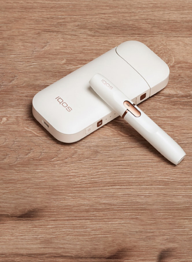 Gold IQOS device, a mobile, a yellow cup and a glass of water on a table bar