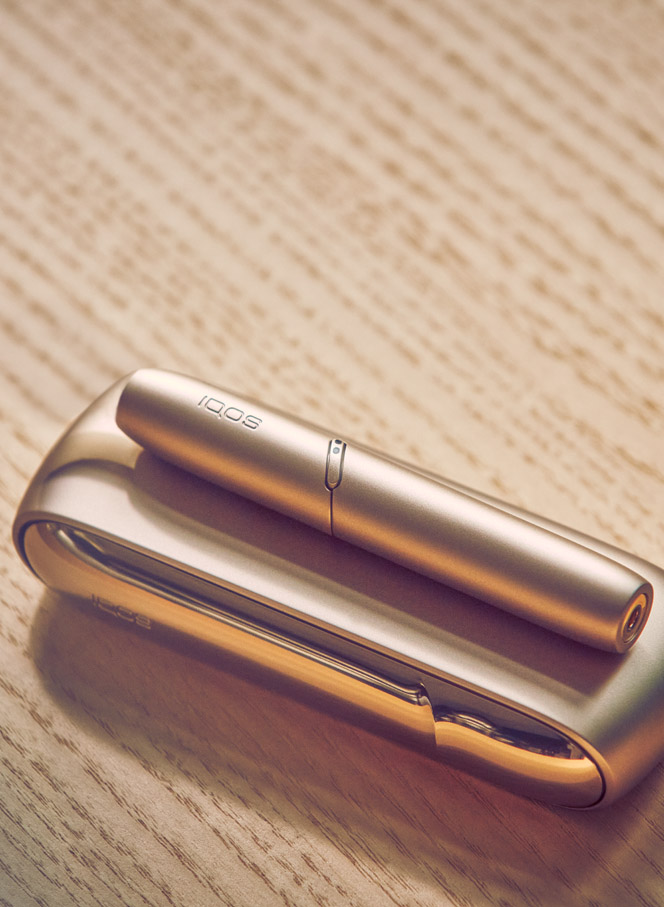 Gold IQOS device, a mobile, a yellow cup and a glass of water on a table bar