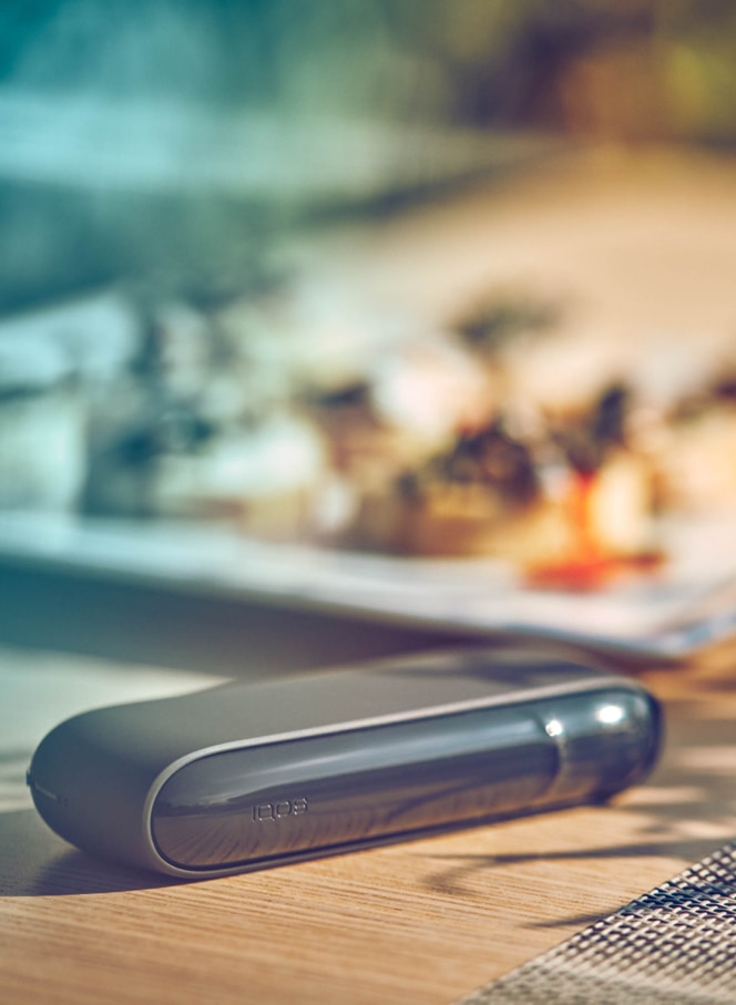 Gold IQOS device, a mobile, a yellow cup and a glass of water on a table bar